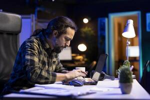 Male creative writer is working remotely, typing away on his laptop at a desk. The concentrated blogger is utilizing online platforms for communication and research, usage of modern technology. photo
