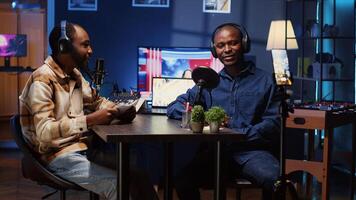 BIPOC host recording entertaining discussion with comedian during podcast filmed in apartment studio with phone on tripod stabilizer. Presenter uses cellphone camera to produce comedy internet show photo