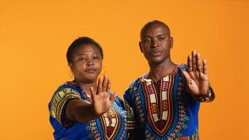 African american couple doing stop symbol with palm, expressing negativity and indicating refuse over orange background. Ethnic married people being displeased with something, warning sign. photo