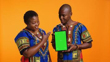 African american married couple holding tablet with greenscreen, pointing at isolated chromakey display on mobile device. Man and woman looking at gadget layout with blank copyspace screen. photo