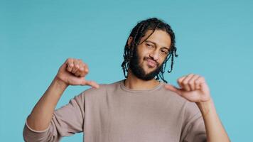 Upset Middle Eastern man showing thumbs down sign gesturing, disapproving, offering negative feedback. Disappointed BIPOC person doing rejection hand gesture, studio background, camera B photo