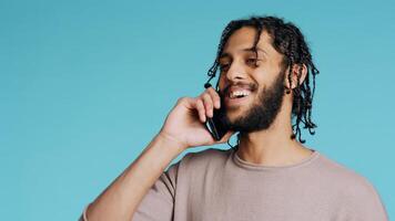 BIPOC man discussing with best friend over telephone call using smartphone. Cheerful person talking with mate in phone call using cellphone, isolated over studio background, camera B close up photo