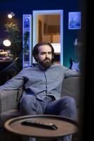 Man watching depressing movie broadcasted on TV, saddened by main character dying at the end. Upset person with teary eyes on couch affected by troubling events in film scene photo