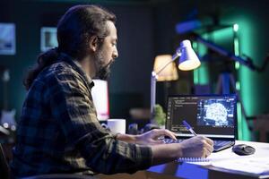 Man at desk using laptop for programming and data analysis. Male programmer working at home, using his notepad while efficiently managing information technology and data center on digital device. photo