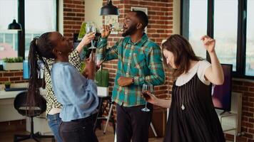 Energetic group of friends dancing at apartment party, having fun together while drinking wine. Multiethnic people doing dance moves on lively music in brick wall living room photo