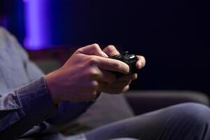 Close up shot of gamepad controller in man hands playing intense online videogame in neon illuminated living room. Gamer participating in internet esports competition, playing on gaming console photo