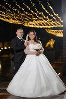 A bride and groom are posing for a picture in front of a lighted backdrop. The bride is holding a bouquet of flowers photo