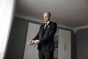 A man in a suit is standing in front of a window, adjusting his tie. Concept of formality and professionalism, as the man is dressed in a suit and tie. The window provides natural light photo