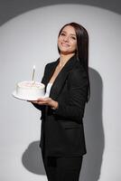 A woman is holding a cake with a candle on it, and she is smiling photo