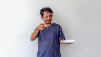 Adult man holding an empty white plate while pointing at it, as if presenting food, isolated on a white background. Perfect for themes related to cooking, food presentation, or meal preparation. photo