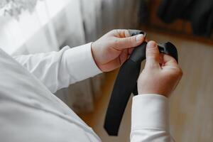 A man is holding a black tie and adjusting it. Concept of formality and attention to detail, as the man is carefully adjusting his tie to ensure it is properly aligned photo