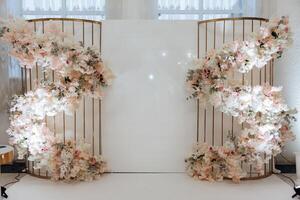 A large white wall with a floral arrangement on it. The arrangement is made up of pink and white flowers, and it is surrounded by a metal frame. The flowers are arranged in a spiral pattern photo