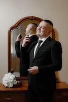 A man in a suit is getting ready for a wedding. He is putting on cologne and adjusting his tie photo