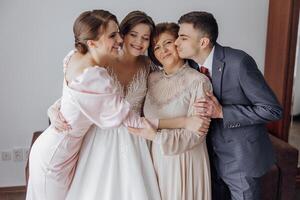 A bride and her three family members are hugging each other. The bride is wearing a white dress and the man is wearing a suit. Scene is warm and loving photo
