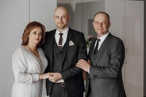 A man and two women are posing for a picture. The man is wearing a suit and tie, and the woman is wearing a dress. Scene is formal and elegant photo