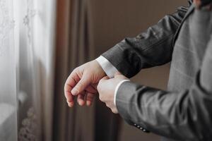 A man is getting dressed in a suit and tie. He is adjusting his tie and putting on his cuff photo
