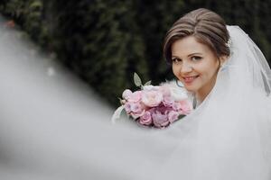 A bride is posing for a picture with a bouquet of pink flowers. She is smiling and looking at the camera photo