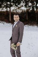 A man in a suit and tie is standing in the snow holding a bouquet of flowers. The scene is serene and peaceful, with the man looking content and happy photo