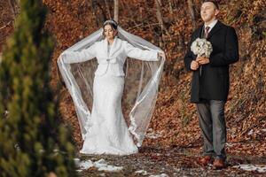 A bride and groom stand in a forest, the bride holding a bouquet. Scene is romantic and serene photo