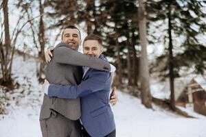 Two men hug each other in the snow. One of them is wearing a blue jacket. Scene is warm and friendly photo