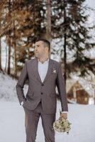 A man in a suit stands in the snow holding a bouquet of flowers. The scene is serene and peaceful, with the man looking out into the distance. The combination of the man's formal attire photo