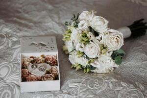 A white bouquet of flowers sits on a bed next to a white box. The box contains a pair of earrings. Concept of elegance and sophistication, as the flowers and earrings are both white and delicate photo