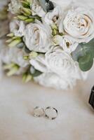 A bouquet of white flowers sits next to a pair of wedding rings. The rings are silver and appear to be a symbol of love and commitment. The bouquet of flowers adds a touch of elegance photo