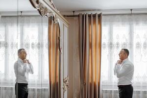 A man is getting ready for a wedding and is adjusting his tie. The image is a reflection of him in a mirror photo