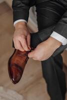 A man is putting on his shoes. The shoes are brown and the man is wearing a suit photo