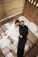 A man and woman are lying on a bed, holding hands and looking at each other. Scene is romantic and intimate photo