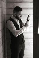 A man in a black vest is getting dressed. He is wearing a watch and has a beard photo