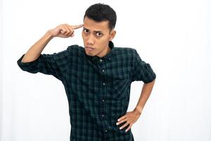 An Asian man wearing a casual green checkered shirt gave off an angry expression while pointing his finger at his brain to tell it to think. Isolated white background. photo