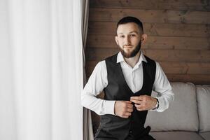 A man in a suit and vest is sitting on a couch. He is adjusting his vest and looking at the camera photo