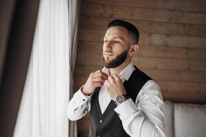 A man in a suit is getting ready to go out. He is wearing a watch and a vest photo