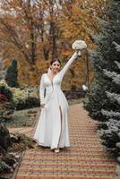 A bride is walking down a brick path with a bouquet of flowers in her hand. The scene is set in a park, with trees in the background. The bride is wearing a white dress and is smiling photo