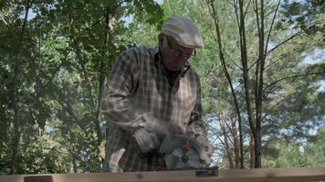 An experienced craftsman is focused on using a power saw to cut wood in a peaceful forest environment. The tranquil surroundings add a unique charm to his meticulous work. video