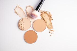 Several samples of different tones of loose powder and two blocks of compact powder with a chic makeup brush. top view. white background. close up. photo
