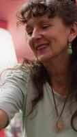 vertical antiguo mujer haciendo su anti envejecimiento diario rutina con protección de la piel productos, mirando en el espejo y aplicando suero y crema a su arrugado rostro. mayor persona utilizando hidratante en su rostro. cámara una. video