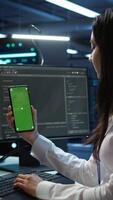 Vertical Worker overseeing data center using green screen mobile phone, ensuring system can handle networking tasks. IT expert in server room tracking network traffic with empty copy space smartphone, camera B video