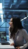 Vertical Engineer in data center sitting down at desk, installing software on computer, troubleshooting issues. Woman arriving at work in server hub, establishing performance benchmarks, camera B video