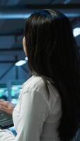 Vertical Data center computer scientist designing, implementing and managing infrastructure to ensure optimal performance and reliability. Woman in server room coding on tablet, camera A video