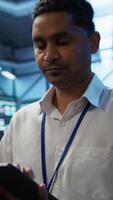 Vertical Software developer walking in data center, managing and maintaining databases, ensuring data integrity and security. Close up of man updating server room mainframe systems using tablet, camera B video