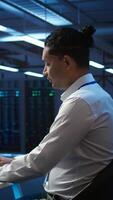 Vertical Portrait of upbeat admin in data center managing servers, operating systems and software programs. Joyous specialist in server hub ensuring networks are secure and functioning properly, camera B video