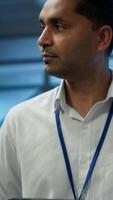 Vertical System administrator walks in data center used for managing gear energy consumption, working on tablet. Close up of IT specialist using device in workspace used for automation in server room, camera A video