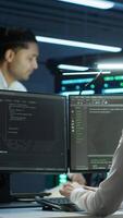 Vertical Team of researchers in data center monitoring security threats using PC, implementing cybersecurity measures. Teamworking colleagues ensuring compliance with regulations, camera A video