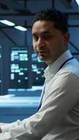 Vertical Portrait of upbeat admin in data center managing servers, operating systems and software programs. Joyous specialist in server hub ensuring networks are secure and functioning properly, camera A video