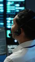 Vertical Data center computer scientist wearing mic headset, doing installation of networking equipment. Server hub IT professional talking in microphone with system administrators, camera A video