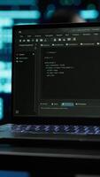 Vertical Close up of code running on laptop screen in data center used for managing gear energy consumption. Focus on notebook used by software developer in blurry background in server farm, camera A video