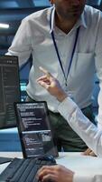 Vertical Team of admins in data center ensuring system can handle networking tasks. Teamworking colleagues in server room tracking network traffic with PC, making improvements, camera B video