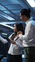 Vertical Team of technicians working on tablets in data center used for managing gear energy consumption. Teamworking colleagues using devices in workspace used for automation in server farm, camera B video